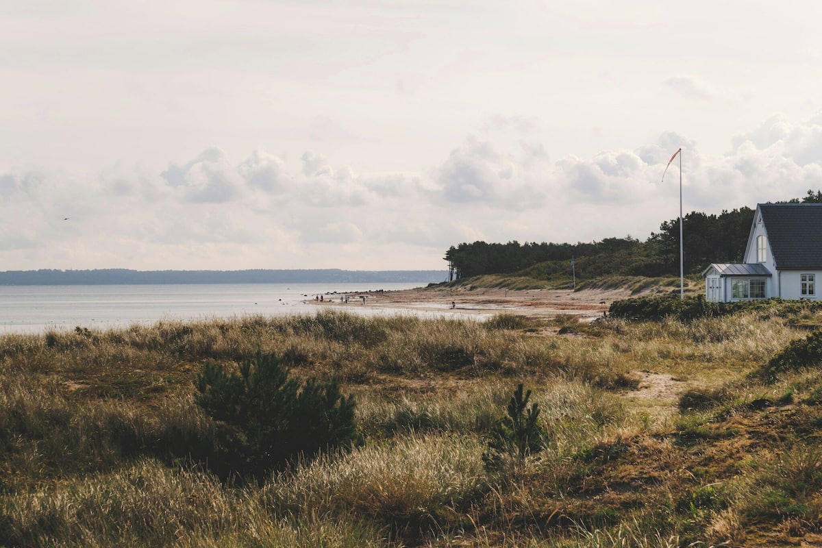 A coastal landscape with a beach, a white building, and a flagpole.