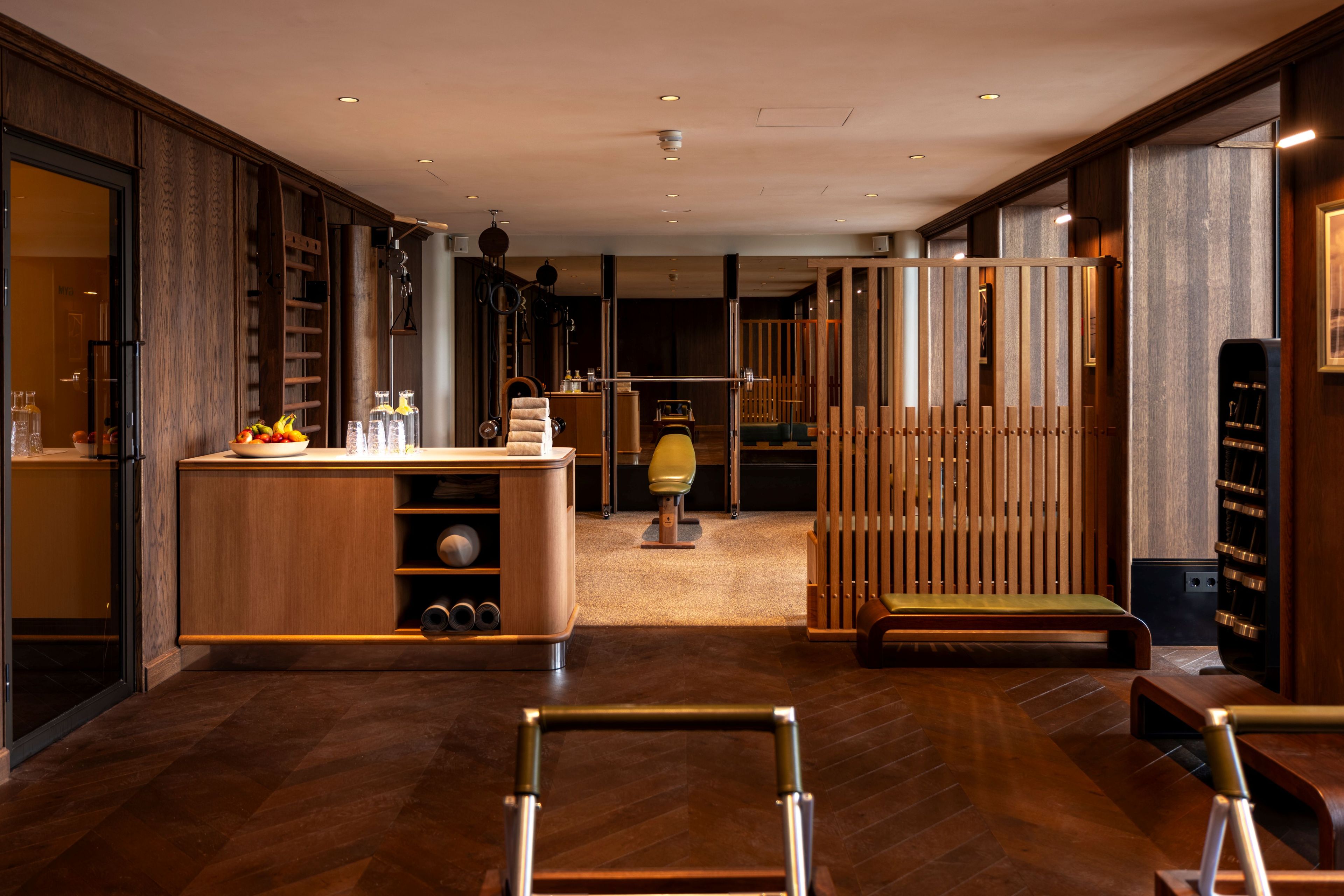 A modern hotel room with a wooden floor, a desk with a bowl of fruit, a chair, and a large window.