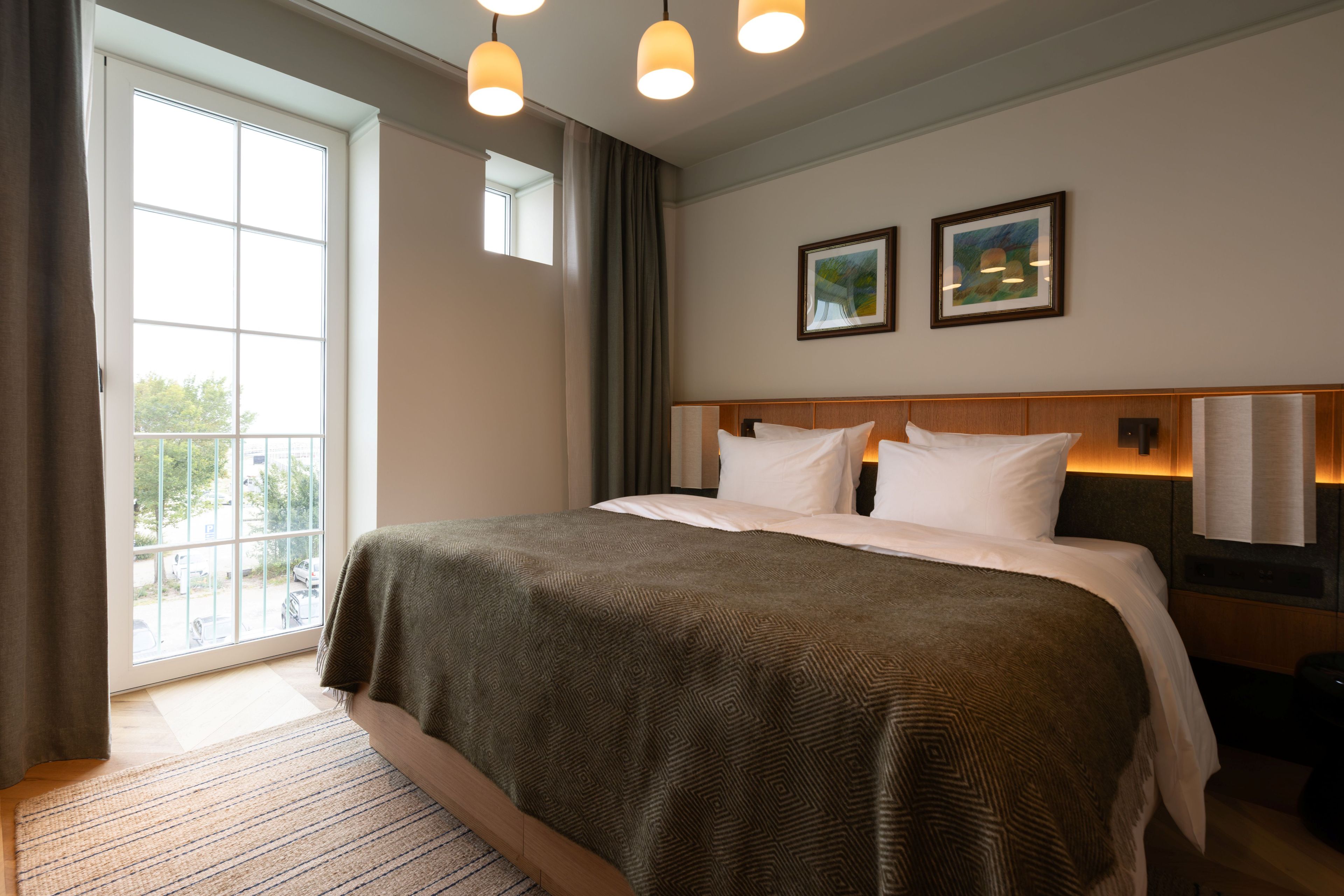 Quarto de hotel com uma cama grande, vista para o exterior e duas fotos emolduradas na parede.