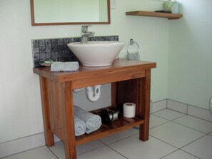 Ein Badezimmer mit einem Holzbadezimmermöbel, einem weißen Waschbecken, einem Spiegel und einem Ablagefach mit Handtüchern und Pflegeprodukten.