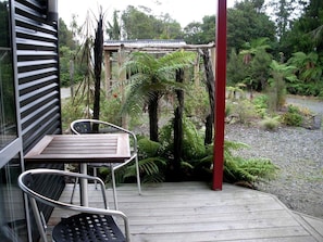 A wooden deck with a table and chairs, surrounded by lush greenery and a red pillar.