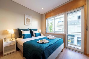 Ein Hotelzimmer mit Bett, Nachttischen, einem Fenster mit Aussicht und einem Gemälde an der Wand.