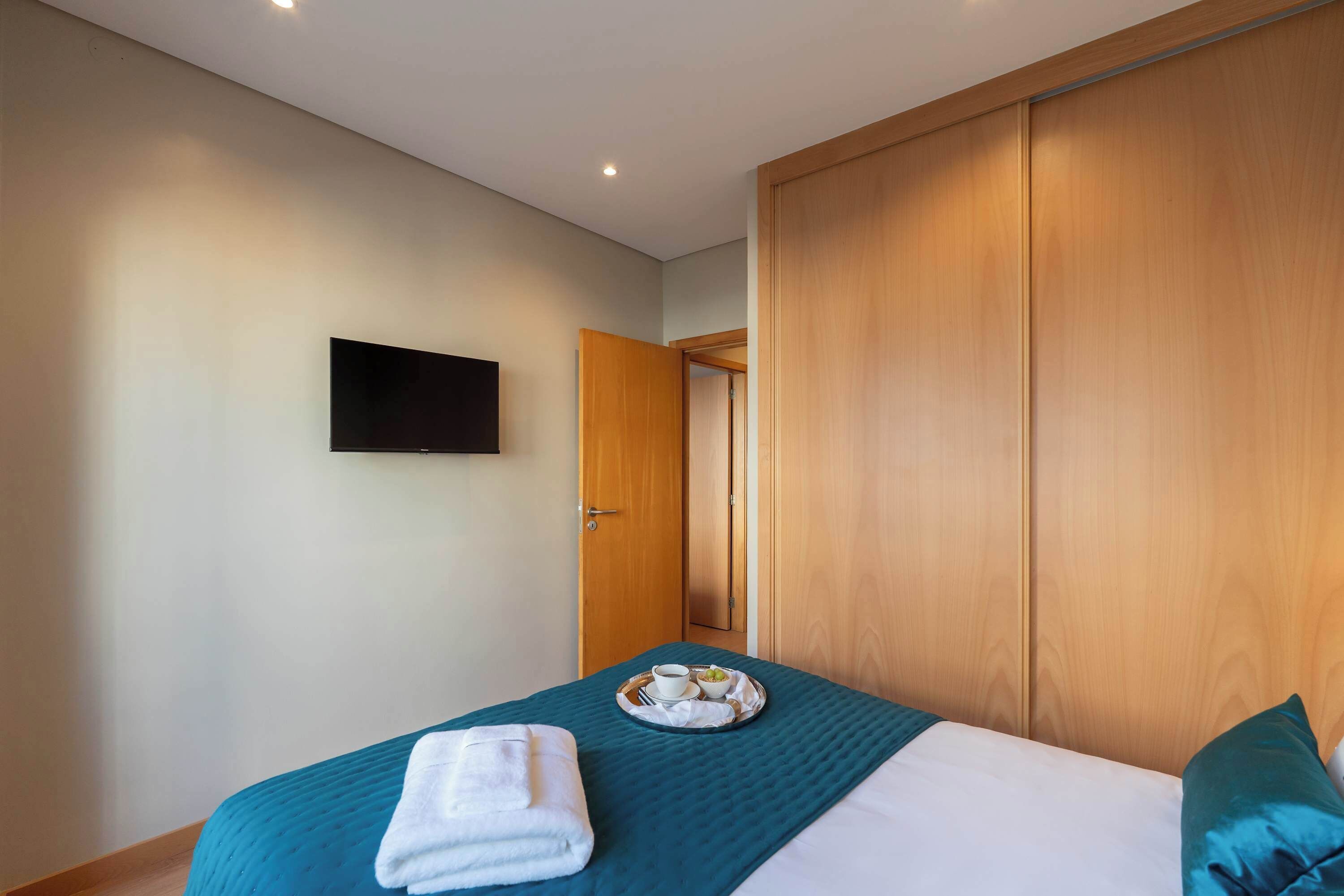 Une chambre d’hôtel avec un lit, un téléviseur  à écran plat fixé au mur et une armoire en bois.