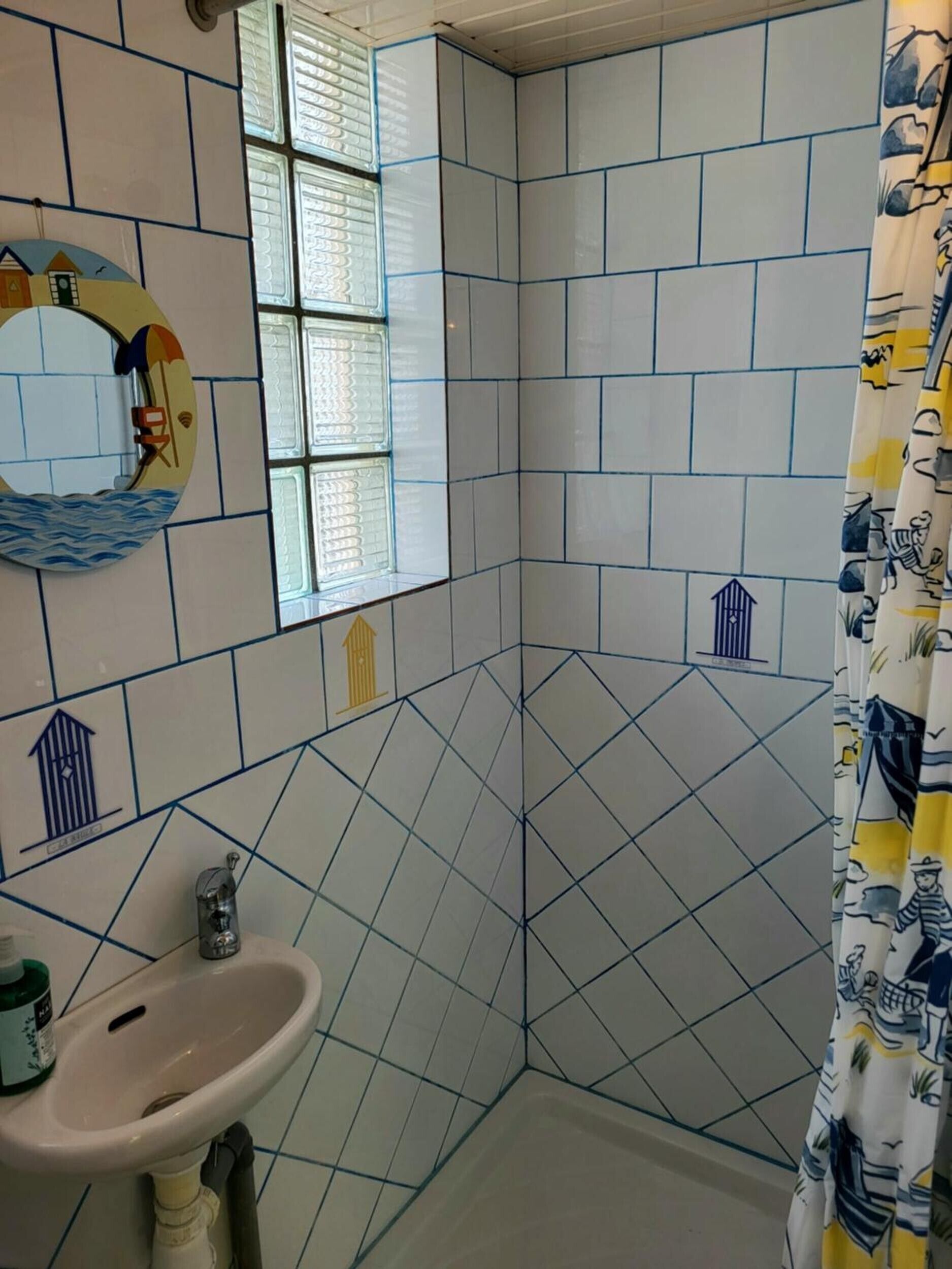 A bathroom with a sink, a window with blinds, and a shower curtain with a nautical pattern.