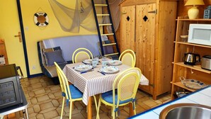 Una habitación acogedora con una mesa de comedor dispuesta para cuatro personas, un sofá, un armario de madera y un microondas en un estante.