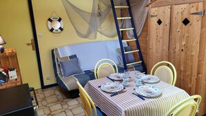 Una habitación acogedora con una cama, una mesa de comedor preparada para cuatro personas y una escalera apoyada en la pared.