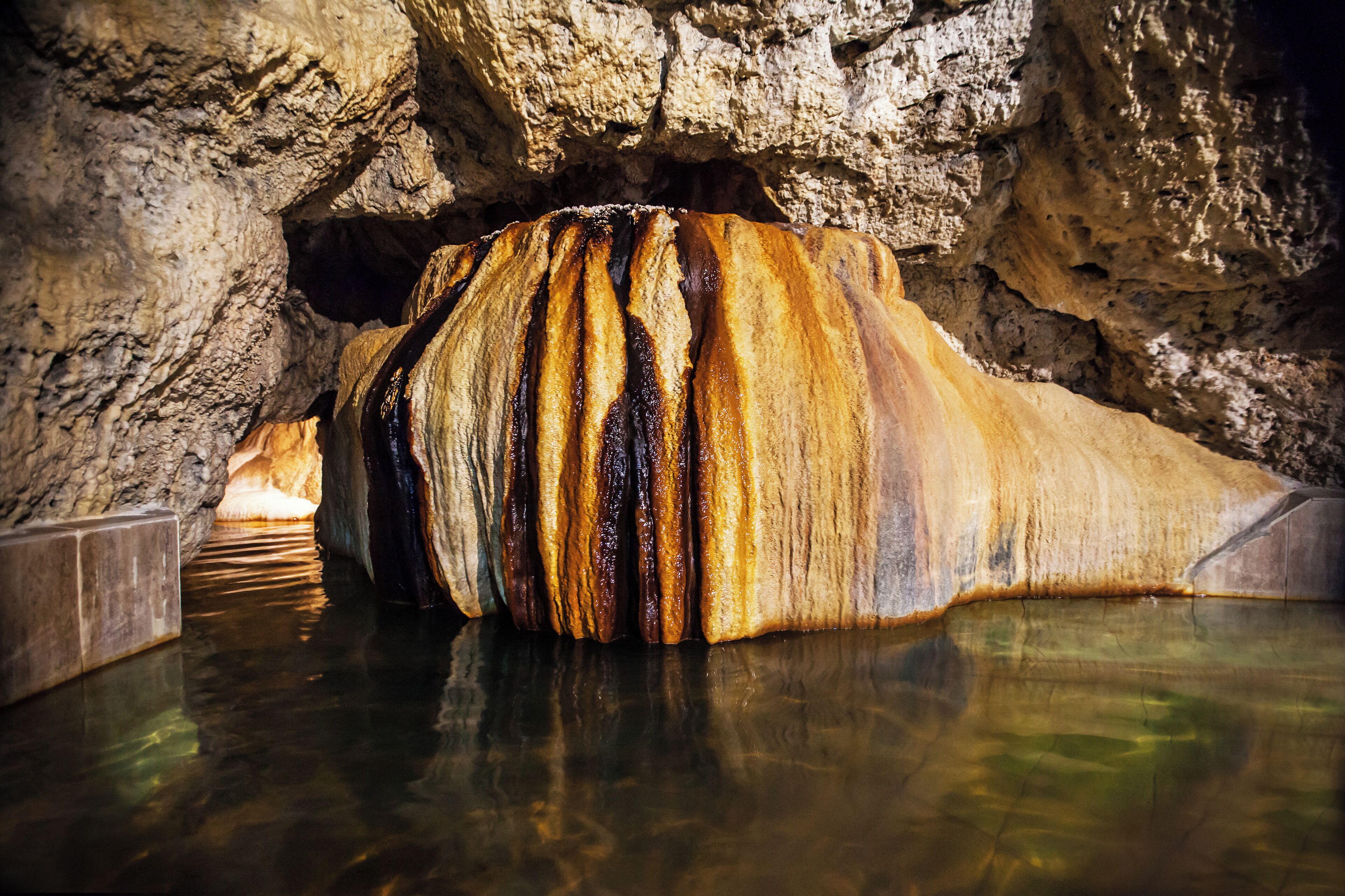 A large rock formation in a cave with water at its base.