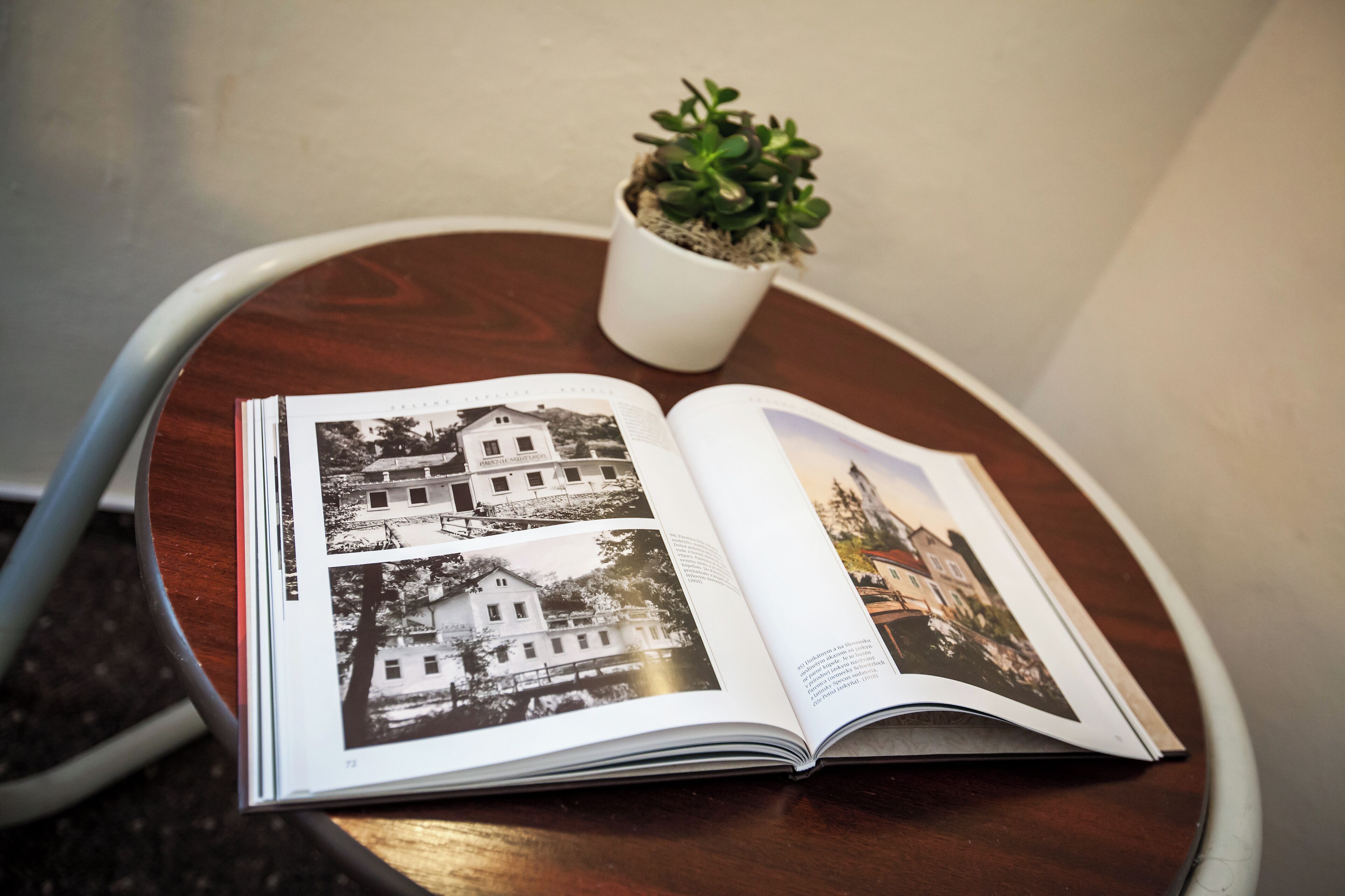 Un livre ouvert, contenant des photographies en noir et blanc de bâtiments, est posé sur une table ronde en bois.