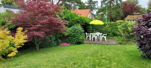 Un giardino con un tavolo e sedie bianche all'aperto, circondato da alberi e arbusti diversi.