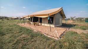 Una tienda safari con un toldo grande, una silla de madera y un farol colgante.