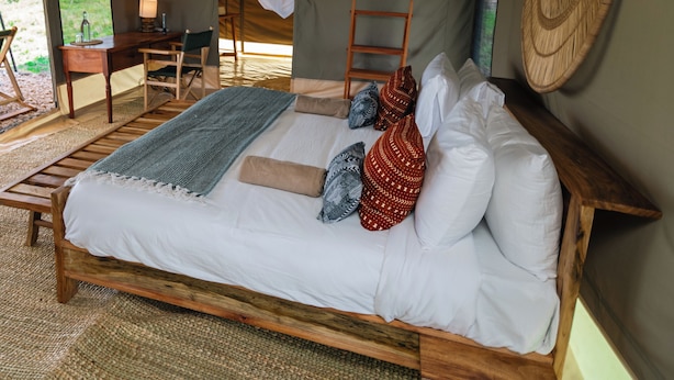 Una tienda de campaña con una cama, una mesa, sillas, una lámpara colgante y una escalera.