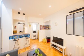 Een compacte leefruimte met een keuken, een eethoek, een televisie en een wasmachine.