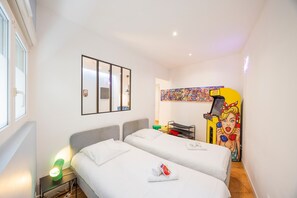 Een hotelkamer met twee bedden, een nachtkastje met een lamp, een spiegel en een kleurrijk kunstwerk aan de muur.