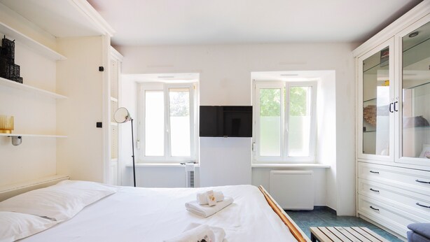 A hotel room with a bed, a wooden bench, a wardrobe, and a television. - Apartment "L'Atelier - Near Train Station" with Wi-Fi (Mulhouse)