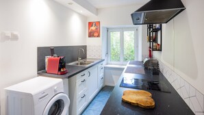 A modern kitchen with a washing machine, a coffee machine, a black countertop, and a window with a view of greenery. - Apartment "L'Atelier - Near Train Station" with Wi-Fi (Mulhouse)