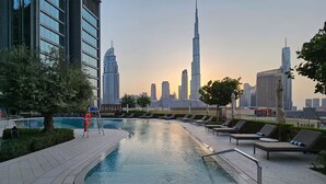 A rooftop pool with lounge chairs, a lifeguard stand, and a view of the Dubai skyline.