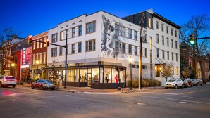 A building with a large mural, storefronts, and parked cars at a street corner.