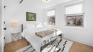 A bedroom with a bed, a bedside lamp, a window, and a painting on the wall.