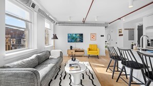 A modern living room with a sofa, coffee table, and chairs, a dining area with a table and chairs, and a kitchen area with a sink and counter.
