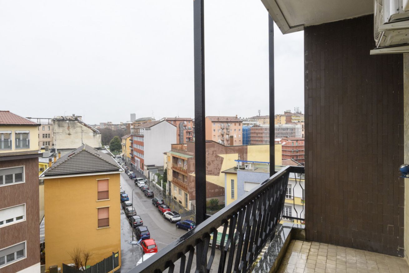 Een balkon met uitzicht op een stadsstraat, gebouwen en geparkeerde auto's.