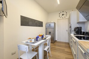 A compact kitchen with a dining table set for two, a refrigerator, and a clock on the wall. - Modica, 16 - Apartment near Iulm (Milan)