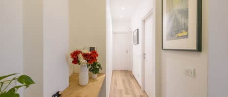 Un couloir avec un banc en bois, un vase rempli de fleurs et un tableau encadré accroché au mur.
