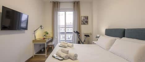 A hotel room with a bed, a desk with a lamp, a TV, and a window with curtains.