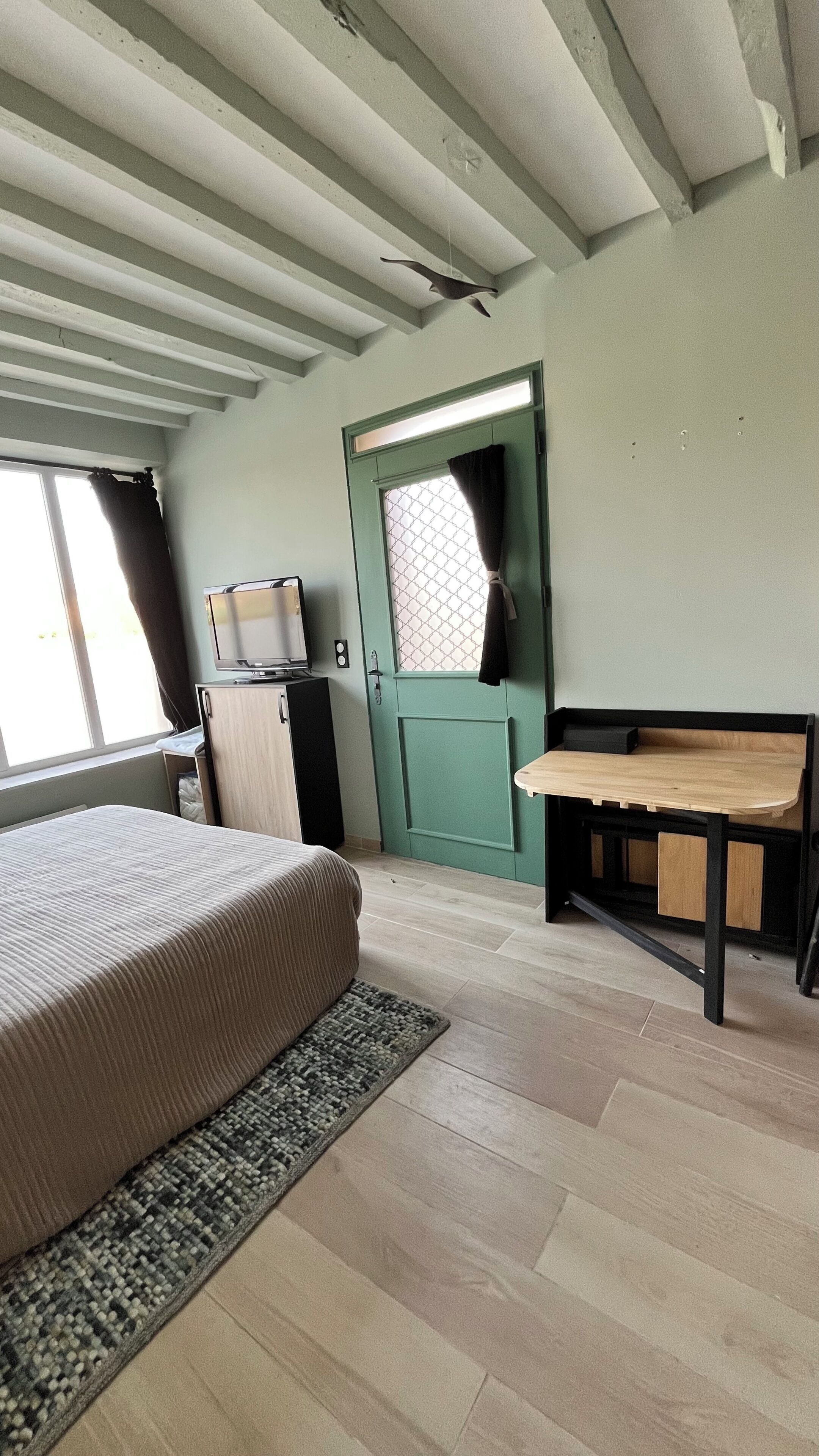 Een kamer met een bed, een bureau, een televisie en een deur met een raam.