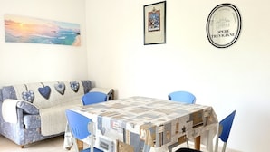A dining area with a table covered in a patterned tablecloth, blue chairs, a sofa with heart-shaped cushions, and a framed picture on the wall. - SE182 - Senigallia, three-room apartment facing the sea with balcony and parking space (Senigallia)