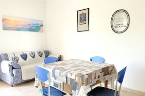 A dining area with a table covered in a patterned tablecloth, blue chairs, a sofa with heart-shaped cushions, and a framed picture on the wall. - SE182 - Senigallia, three-room apartment facing the sea with balcony and parking space (Senigallia)