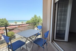 Un balcon avec une table et des chaises, une vue sur la mer et une porte ornée d’un rideau à motifs.