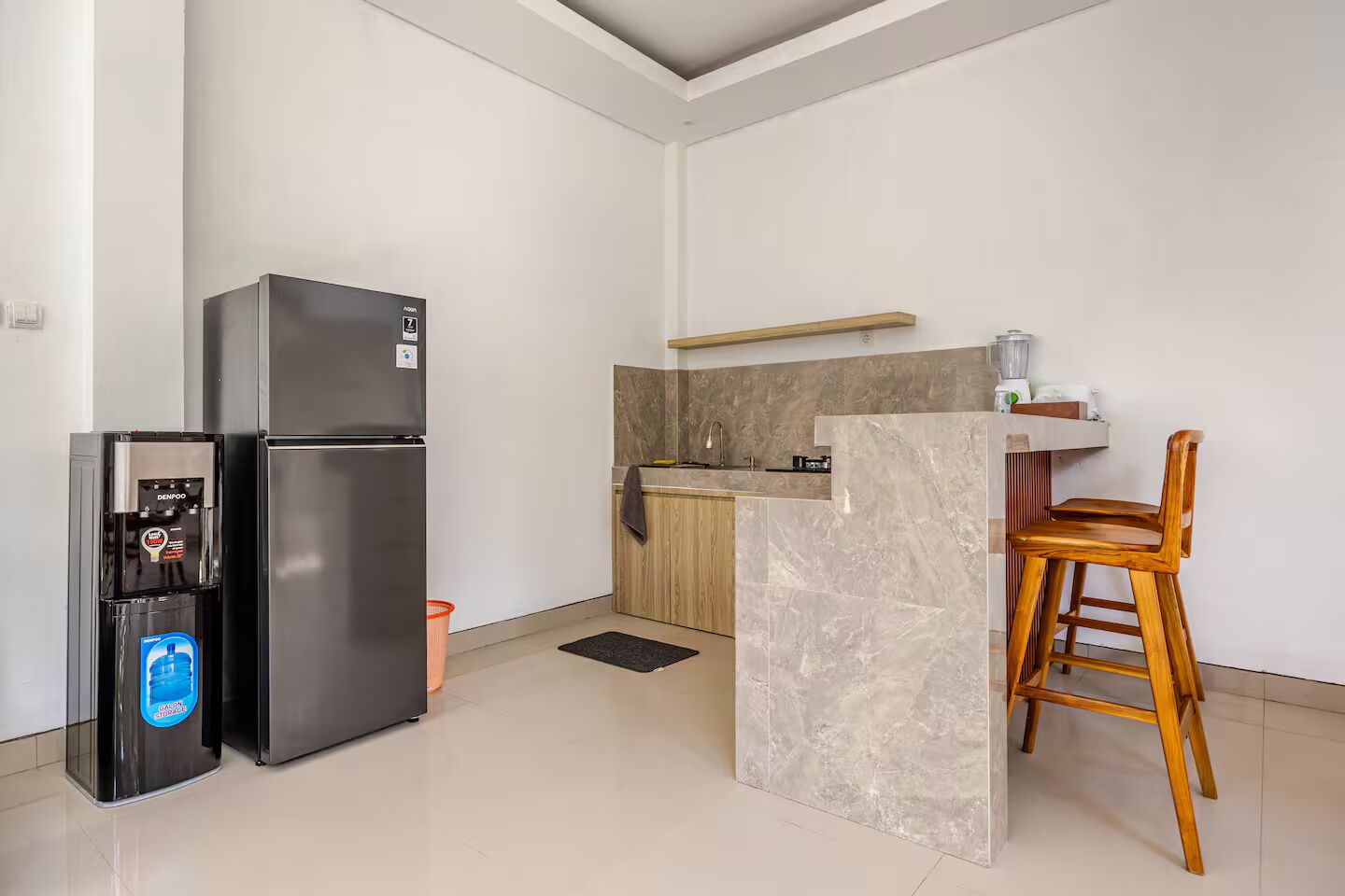 Una cocina moderna con refrigerador, dispensador de agua, una silla de madera y encimera de mármol.