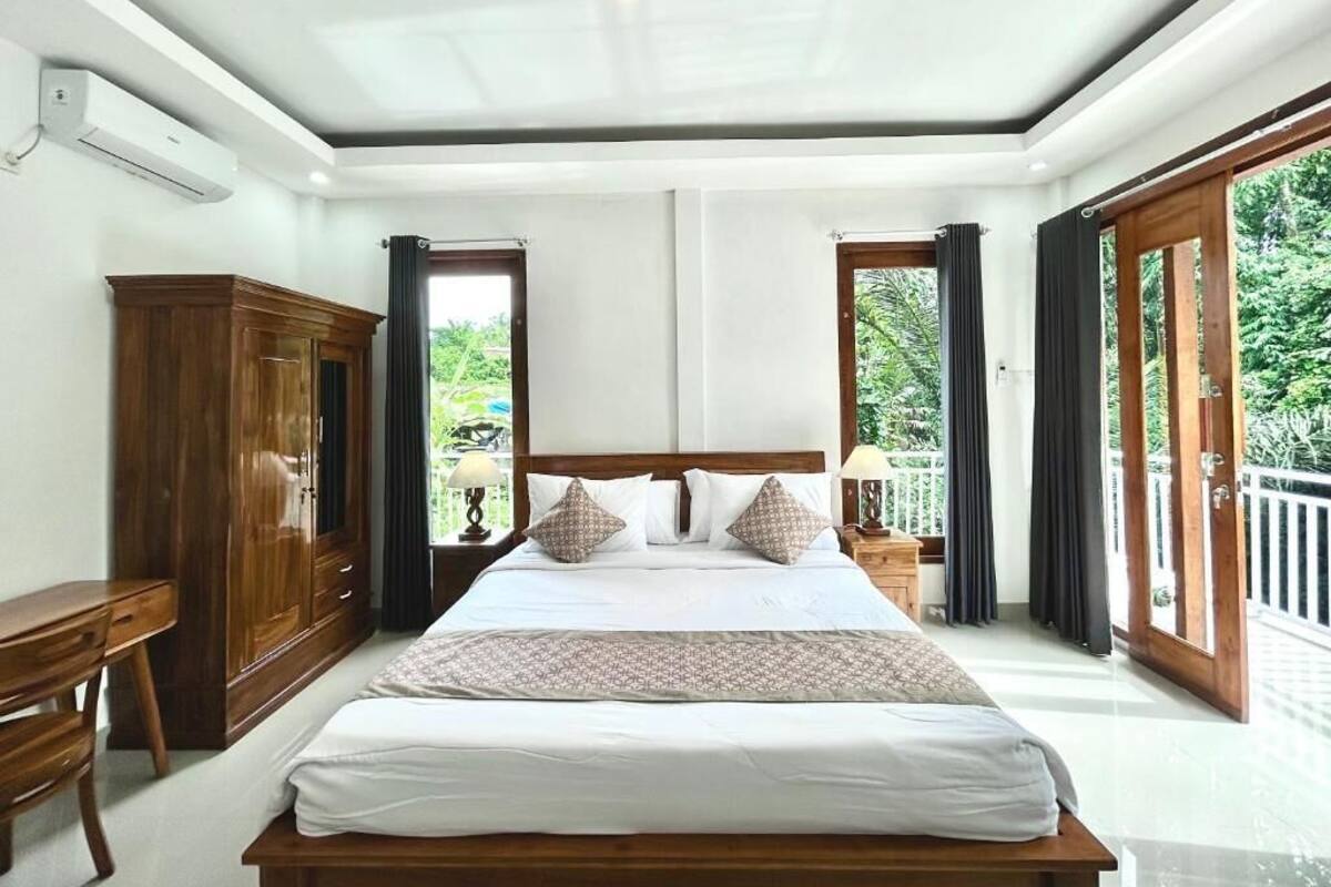 Een slaapkamer met een groot bed, een houten kledingkast en uitzicht op groen door de ramen.