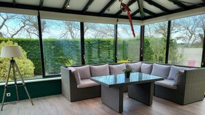 Une véranda dotée d’une table en verre et de sièges rembourrés, entourée de grandes fenêtres.