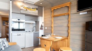 A compact kitchen with a dining area, wooden walls, and a flat-screen TV. - Cozy Ski-In/Ski-Out Studio 26 m² – Alpe d’Huez (Huez)