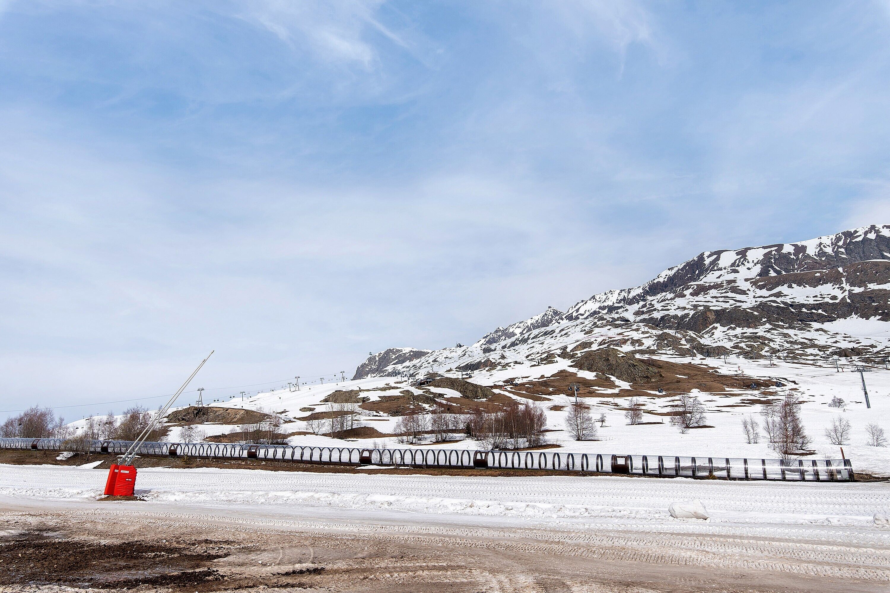 A snowy landscape with a train track, mountains, and a red object in the foreground.