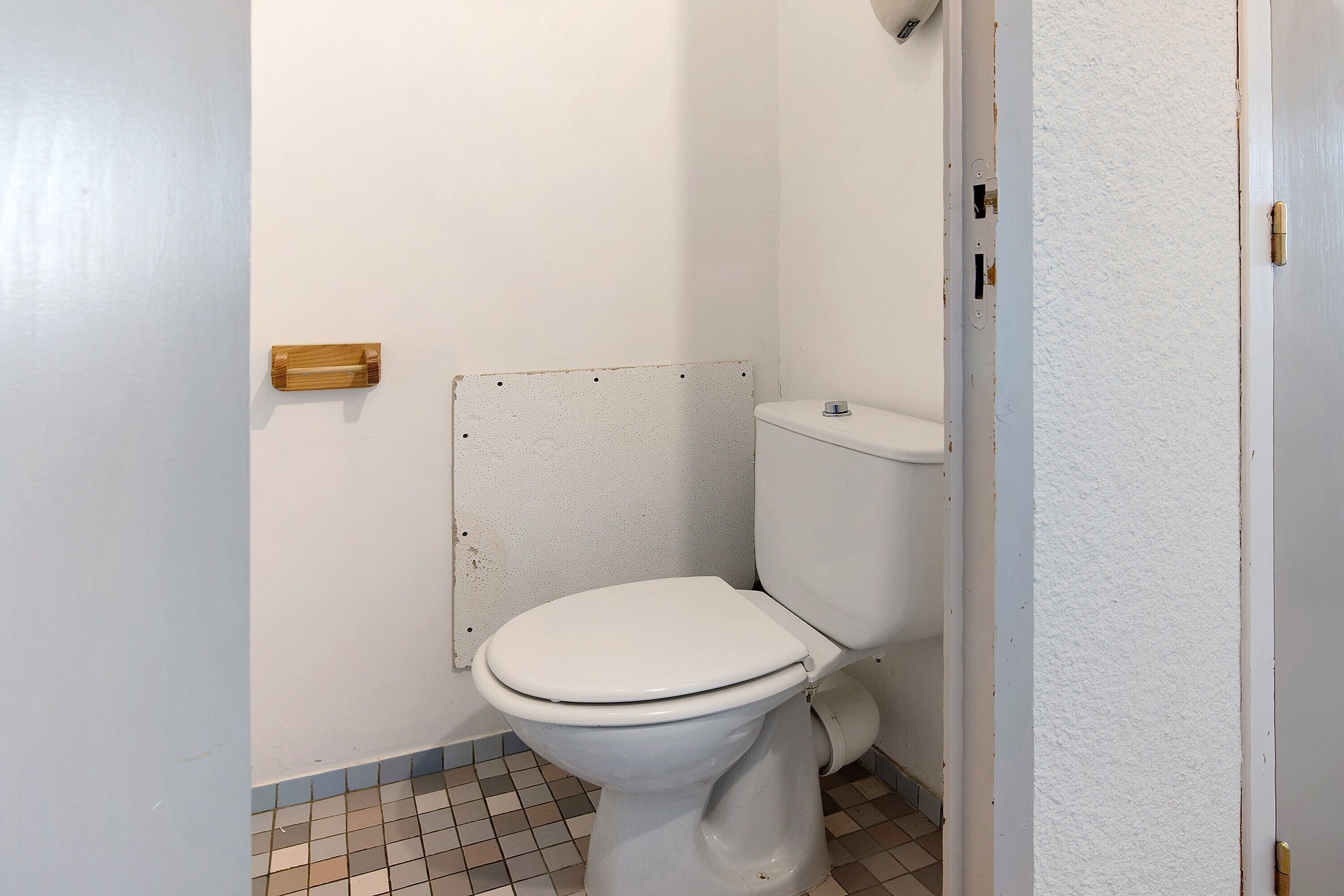 A white toilet with a wooden handle, a white wall, and a tiled floor.