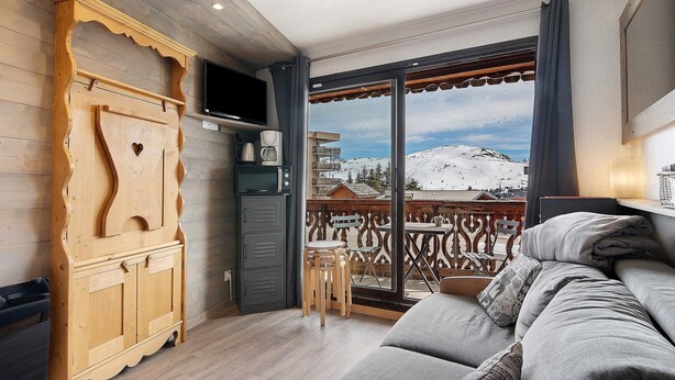 A balcony with a wooden railing, a sofa, and a television. - Cozy Ski-In/Ski-Out Studio 26 m² – Alpe d’Huez (Huez)