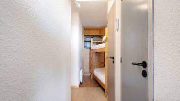 Um corredor estreito com uma cama beliche e uma porta à direita.