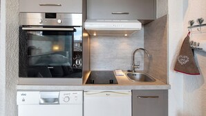 A kitchen with a built-in oven, a dishwasher, a sink, and a stainless steel faucet. - Cozy Ski-In/Ski-Out Studio 26 m² – Alpe d’Huez (Huez)
