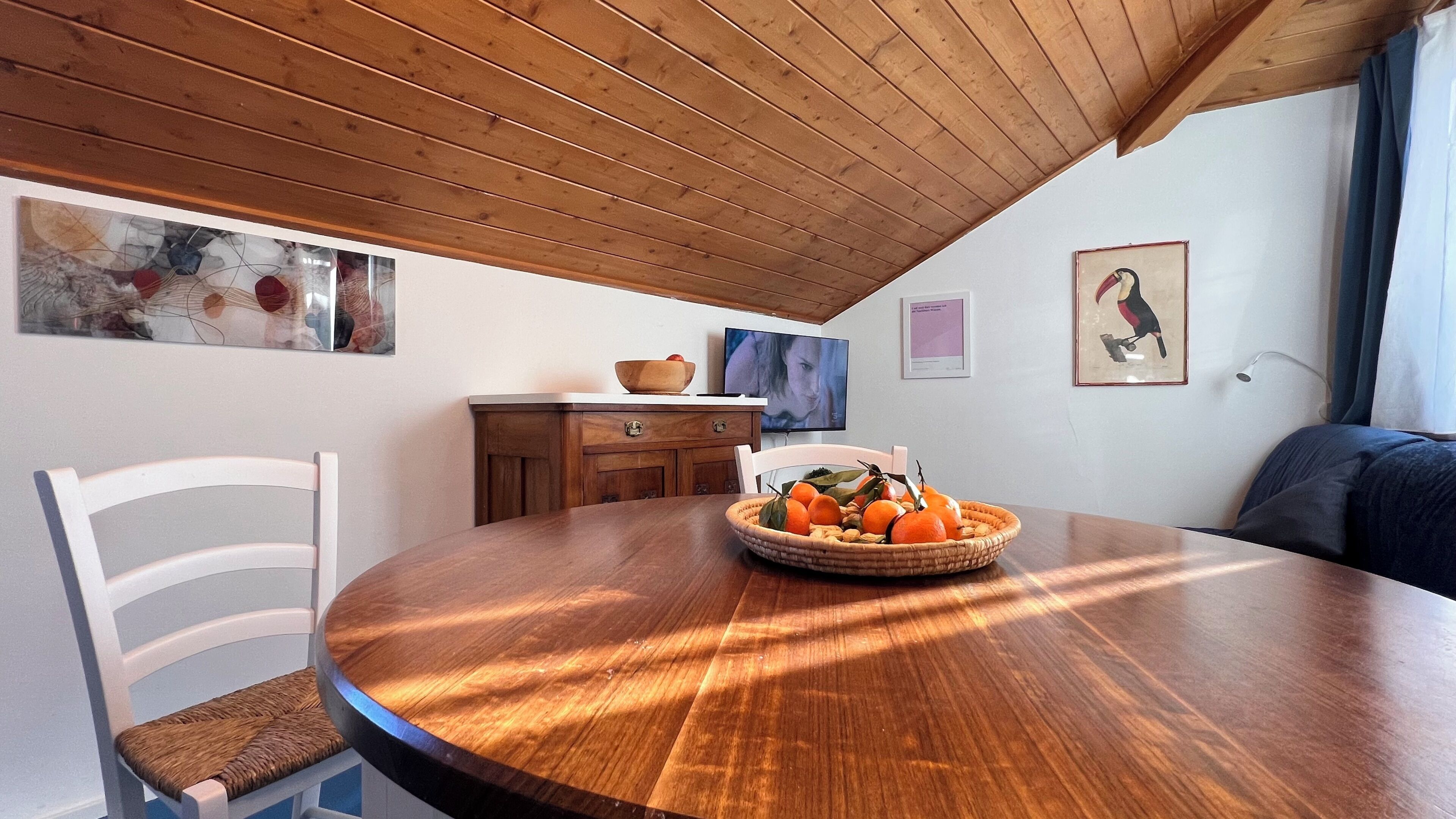 Een eethoek met een houten tafel, witte stoelen en een schaal fruit.