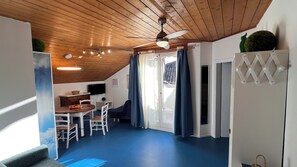 Una habitación acogedora con techo de madera, ventilador de techo, mesa de comedor con sillas, televisor y puerta corrediza de vidrio hacia el exterior.