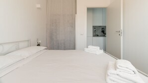 Ein sauberes, modernes Hotelzimmer mit einem ordentlich bezogenen Bett, einem Badezimmer mit Dusche und einer kleinen Küchenzeile.