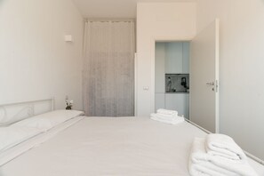 Ein sauberes, modernes Hotelzimmer mit einem ordentlich bezogenen Bett, einem Badezimmer mit Dusche und einer kleinen Küchenzeile.