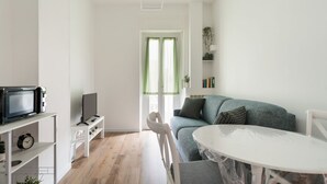 Ein modernes Wohnzimmer mit einem weißen Sofa, einem runden Tisch, einem Fernseher auf einem Schrank und einem Bücherregal.