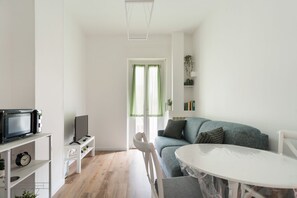 Ein modernes Wohnzimmer mit einem weißen Sofa, einem runden Tisch, einem Fernseher auf einem Schrank und einem Bücherregal.