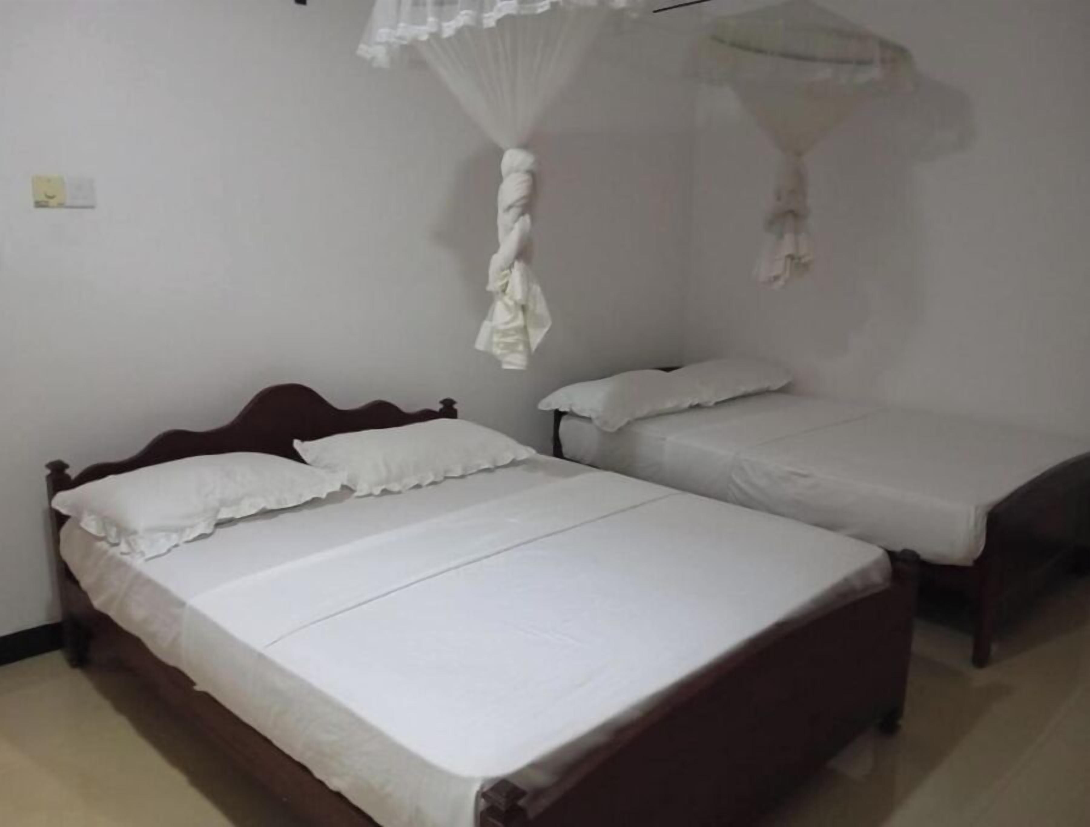 A room with two single beds, a wooden headboard, a white canopy, and a plain wall.