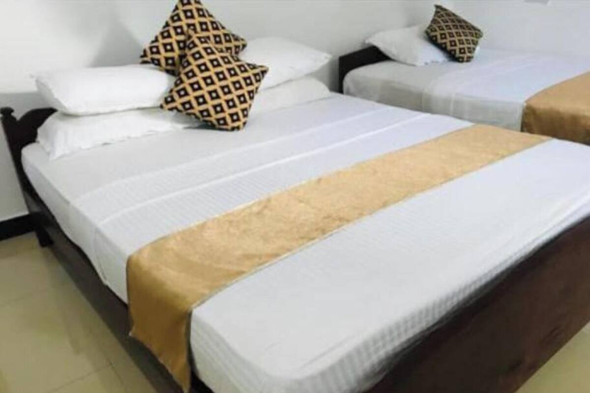 A hotel room with two single beds, each with a white bedspread and a patterned pillow.