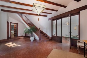 Un intérieur spacieux avec un escalier en bois, une grande plante en pot et un coin repas comprenant des chaises et une table.