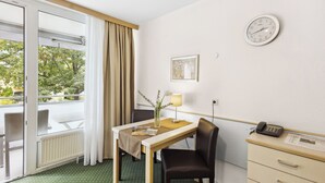 A hotel room with a table, chair, lamp, clock, and a desk with a phone. - Cozy and quiet vacation apartment in the center of Bad Füssing (Bad Füssing)